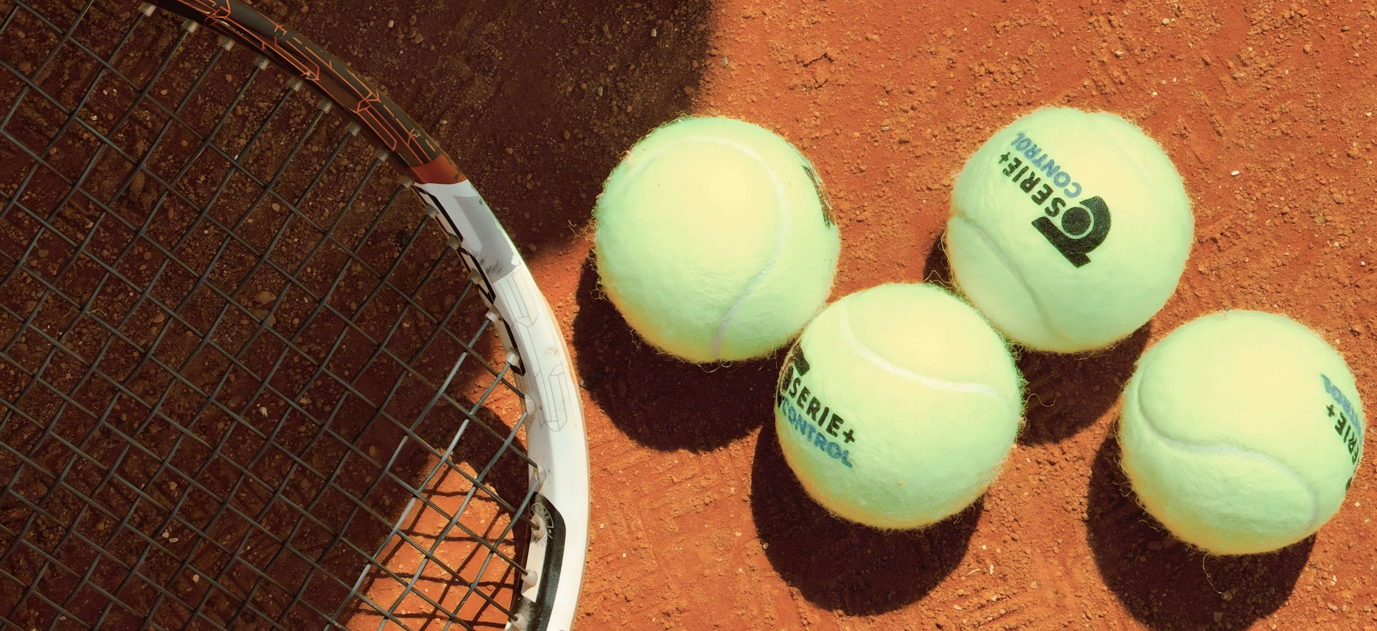 Balles de tennis et raquette posées sur un court en terre battue