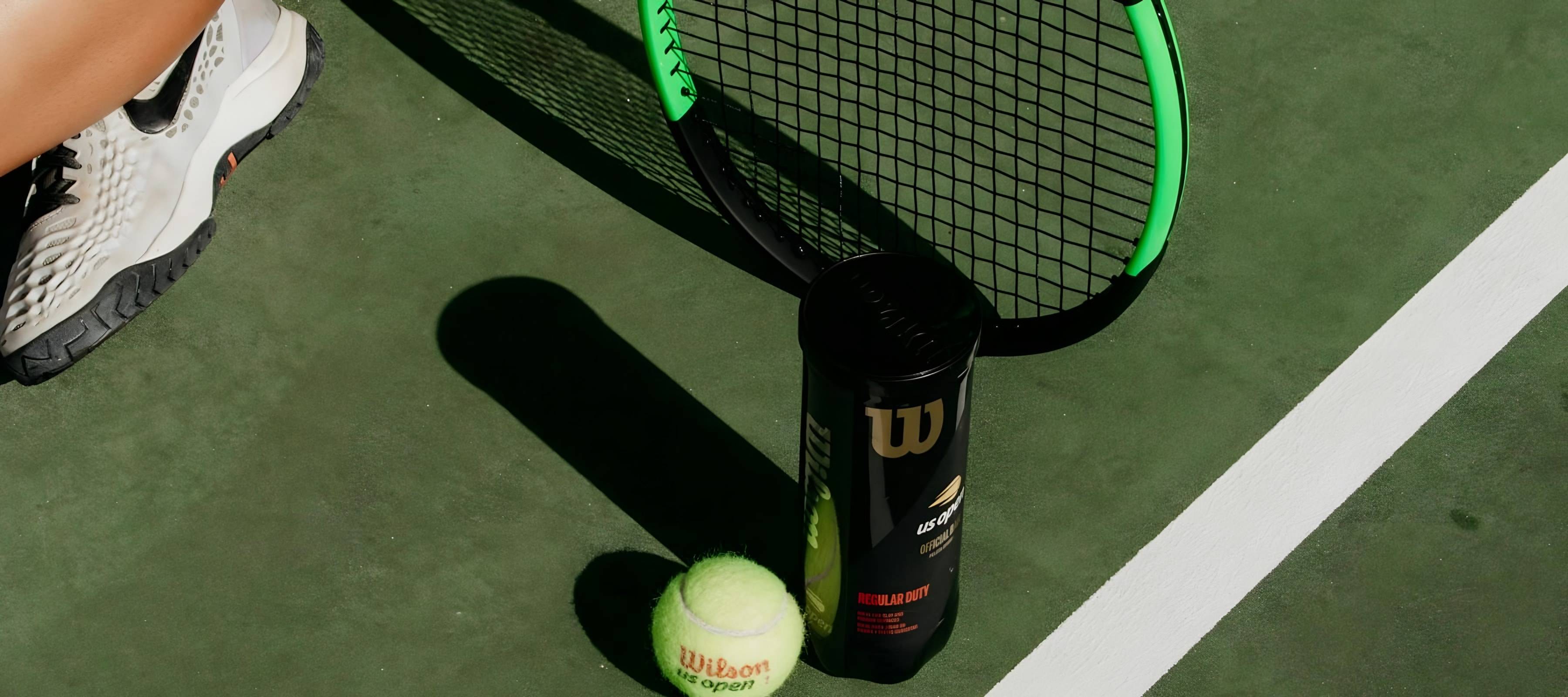 Raquette, tube de balles et balles de tennis posés sur un court